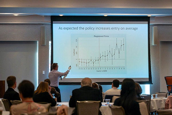 A man standing in front of a screen showing a graph with audience members shown from the back of the room.
