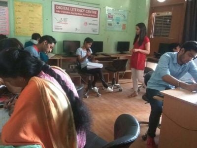 A picture of Sanchita Mehrotra standing in the midst of young adults in a classroom with computers.