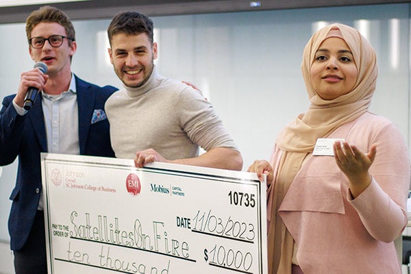 Two men and one woman standing and holding a novelty check for $10,000 made out to Satellites on Fire.