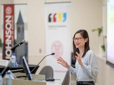 Photo of Simone Tang at a lectern with hands outstretched.