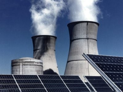 Solar panels with industrial smoke stacks behind them