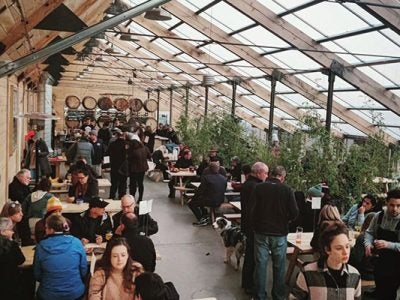 People enjoying food sitting at wooden picnic tables under a greenhouse-style roof at Stone Bend.