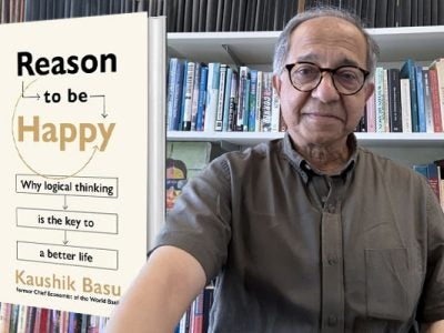 Man stands in front of a book shelf and to his left is an enlarged image of the book he authored.