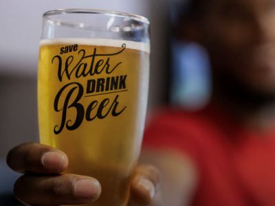 A man holds out a beer glass reading “save water drink beer”