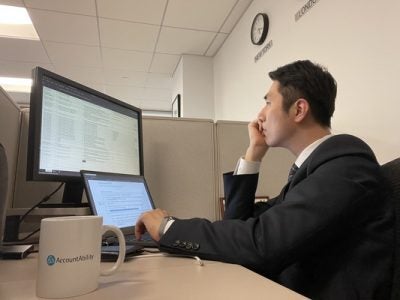 A picture of Duncan Lee working at his cubicle at the NYC office, with an AccountAbility mug.