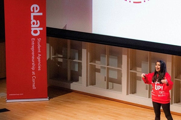Trishala Dessai on stage, speaking and gesturing. An eLab banner is also on stage.