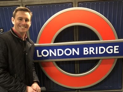 A student poses for a photo with a London Underground metro sign that reads “London Bridge.”
