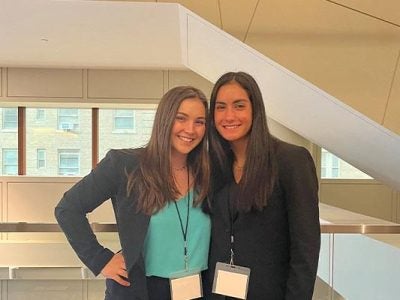 Two women stand smiling at the camera.