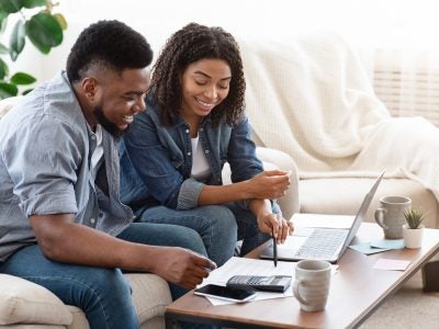 A young, happy couple budget together on their couch.