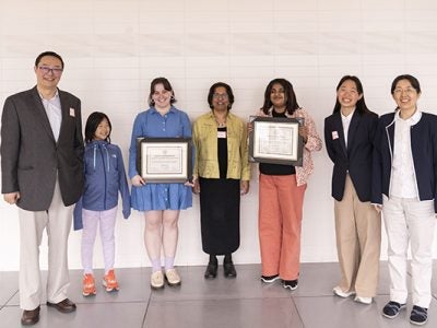 The Ye Family, father, mother and two young daughters, smile for a posed photo with the associate director of graduate programming and two female graduate students who are holding their award certificates