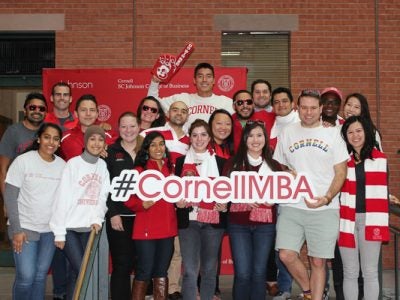 Johnson student MBA ambassadors holding a large #CornellMBA sign