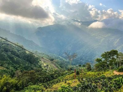 Tree-covered mountainous landscape with dramatic clouds and sun rays, Columbia.