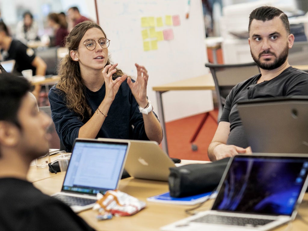 A young woman in glasses speaks while leading a collaborative project session with classmates as part of the Johnson Cornell Tech MBA program at Cornell Tech's campus on Roosevelt Island, NYC