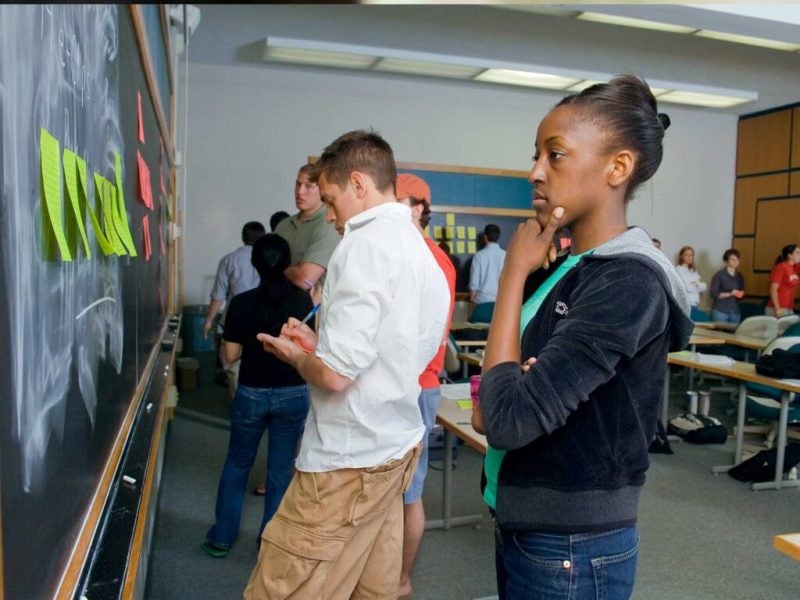 Students work on a project board with colorful sticky notes in a classroom
