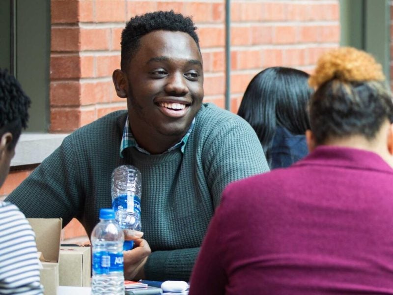 Several students sit outside at a table during lunch and share a meal while talking and laughing