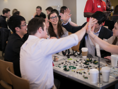 Students high-five over a table of LEGO