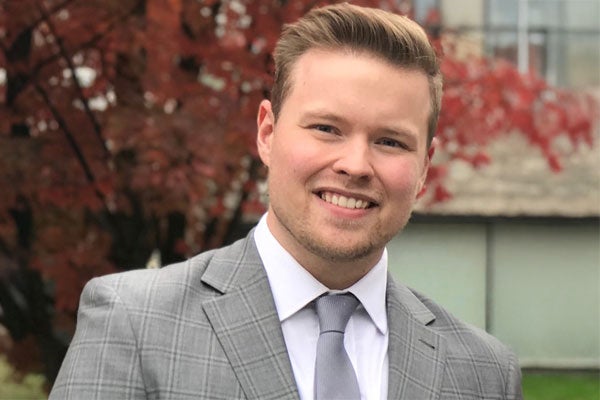MBA student, Douglass Scandrett, in a gray suit smiling outdoors on campus.