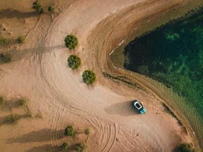 an aerial view of single car on a sandy dirt road.