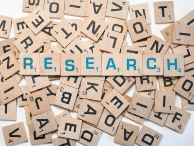 A scattered pile of wooden Scrabble tiles, one alphabet letter on each tile, with the word “research” spelled out on tiles place on top