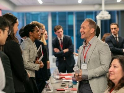 Students and executives talk with a table between them.