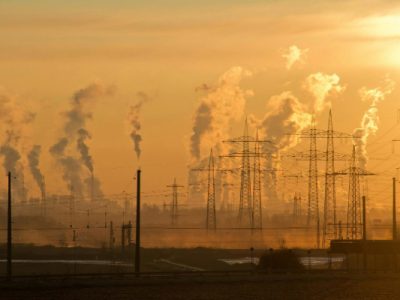 Smoke stacks and electrical wires are shown at a distance amid the yellow orange glow of the sunset.