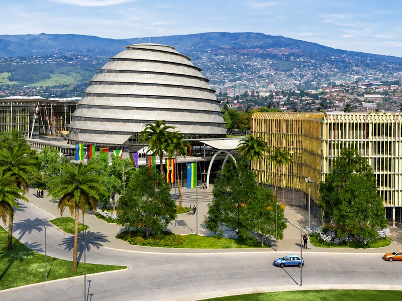 Rendering of the Hanga Ahazaza initiative campus in Kigali, Rwanda, featuring a modern dome-shaped building, surrounding academic structures, palm-lined streets, and mountainous landscape in the background.