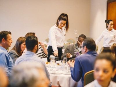 Photo of a girl pouring coffee to a table of guests at Hotel Ezra Cornell