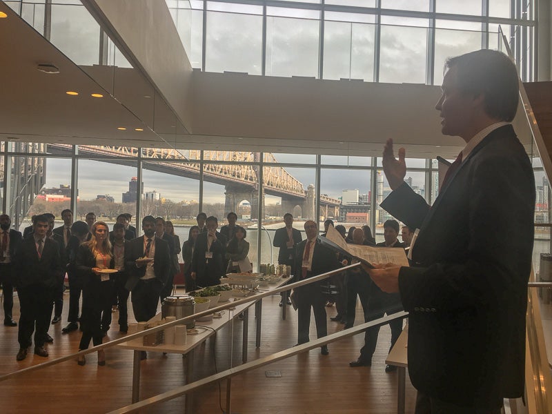 Scott speaking to a large reception with the NYC skyline outside of the window