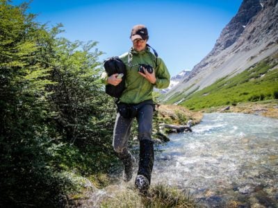 A man crosses a stream in a rugged landscape
