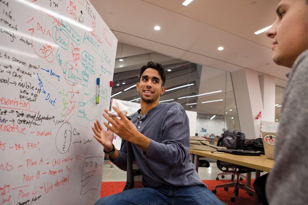 Two young men collaborate while using a densely populated white dry erase board in a Studio space at Tata Innovation Center at Cornell Tech's Roosevelt Island campus