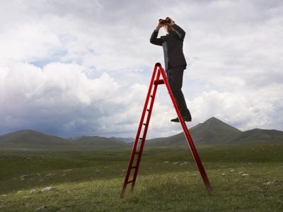 Businessman on ladder looking through binoculars