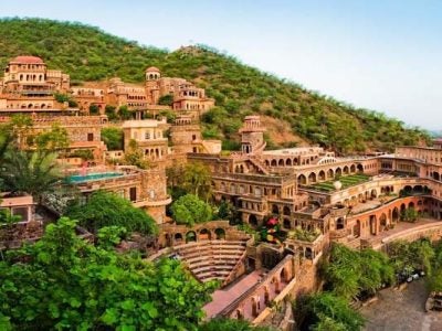 Exterior photo of the Neemrana Fort-Palace resort property. The photo depicts an imposing fort-like structure built into a lush hillside.