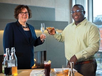 Cheryl Stanley and Douglass Miller clink glasses near a bar cart with cocktail ingredients.