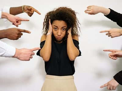 A young, frustrated woman with several hands pointing their fingers at her