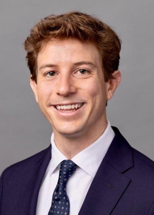 Pietro Bini, a Ph.D. in Management graduate from Cornell, smiles at the camera in business formal attire against a gray background