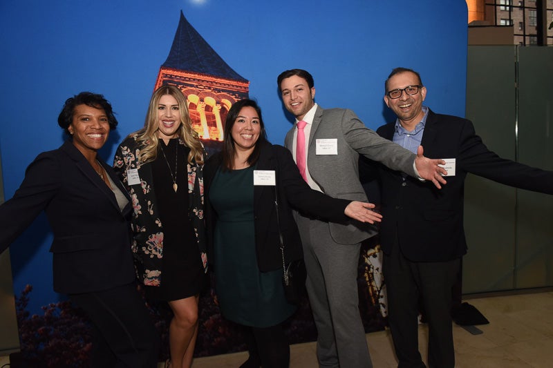 Photo of alumni standing in front of the Sage Hall backdrop