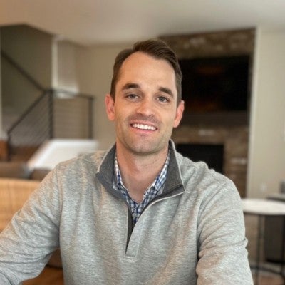 Riley Watts, Cornell MBA Class of 2022, dressed in business casual attire within a home setting, smiles at the viewer