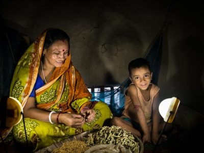 A woman and child sit next to a solar lamp in a tent