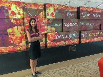 Photo of Sonal Lakhotia standing in front of a display that reads: When different people come together, it's not just beautiful, it's priceless