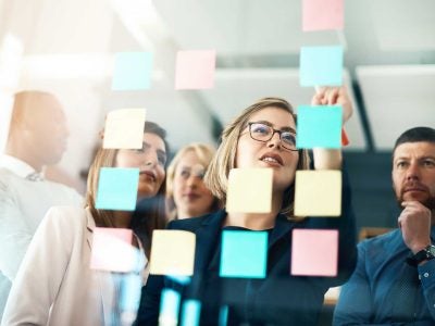 Colleagues look at post it notes on a glass board.