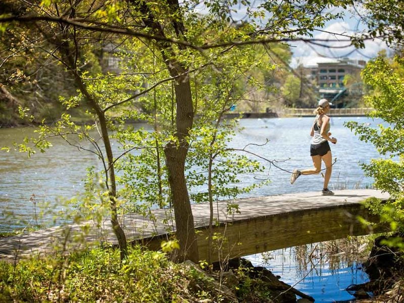 Woman runs across foot bridge with Beebe Lake visible in background and greenery in foreground