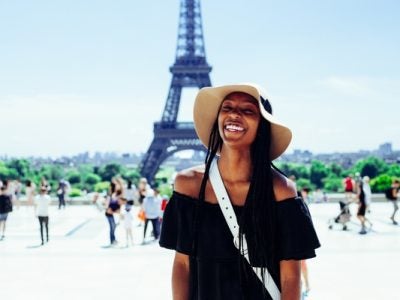 A young woman tourist smiles in front of the Eiffel Tower in Paris, France.