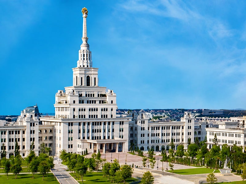 View of VinUniversity in Hanoi, Vietnam, featuring a large white neoclassical academic building with a tall central spire under a bright blue sky.