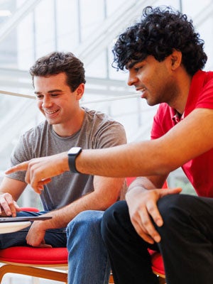 Two students sitting together and reviewing work on a tablet, one pointing at the screen as the other smiles.