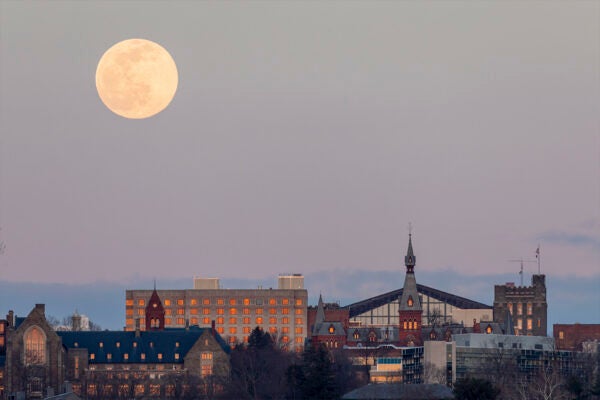 Dusk view of Cornell University campus including Statler Hall with a large full moon glowing above in the sky