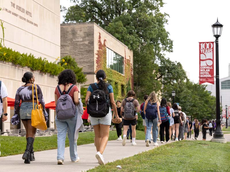 Students walking on sidewalk on Feeney Way in front of Statler Hall