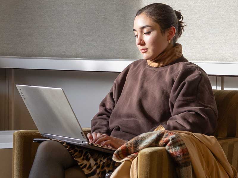 Female student sitting in chair working on laptop
