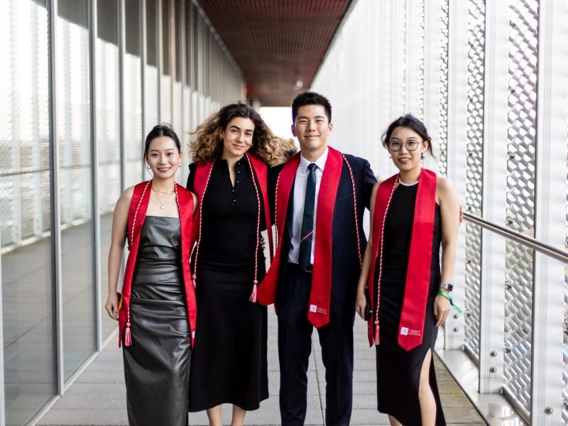 4 students standing outdoors in graduation regalia