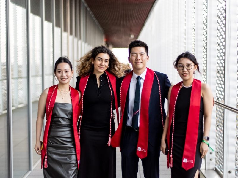 4 students standing outdoors in graduation regalia
