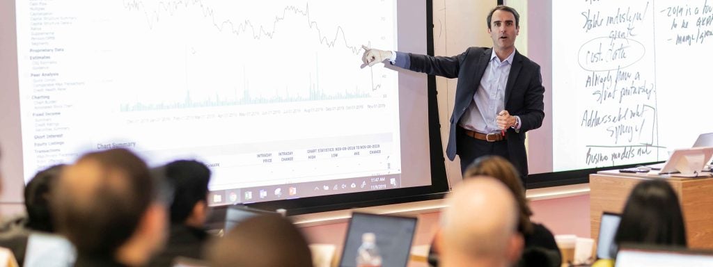 Cornell SC Johnson College of Business college faculty in front of class, pointing to whiteboard with some sort of downward graph